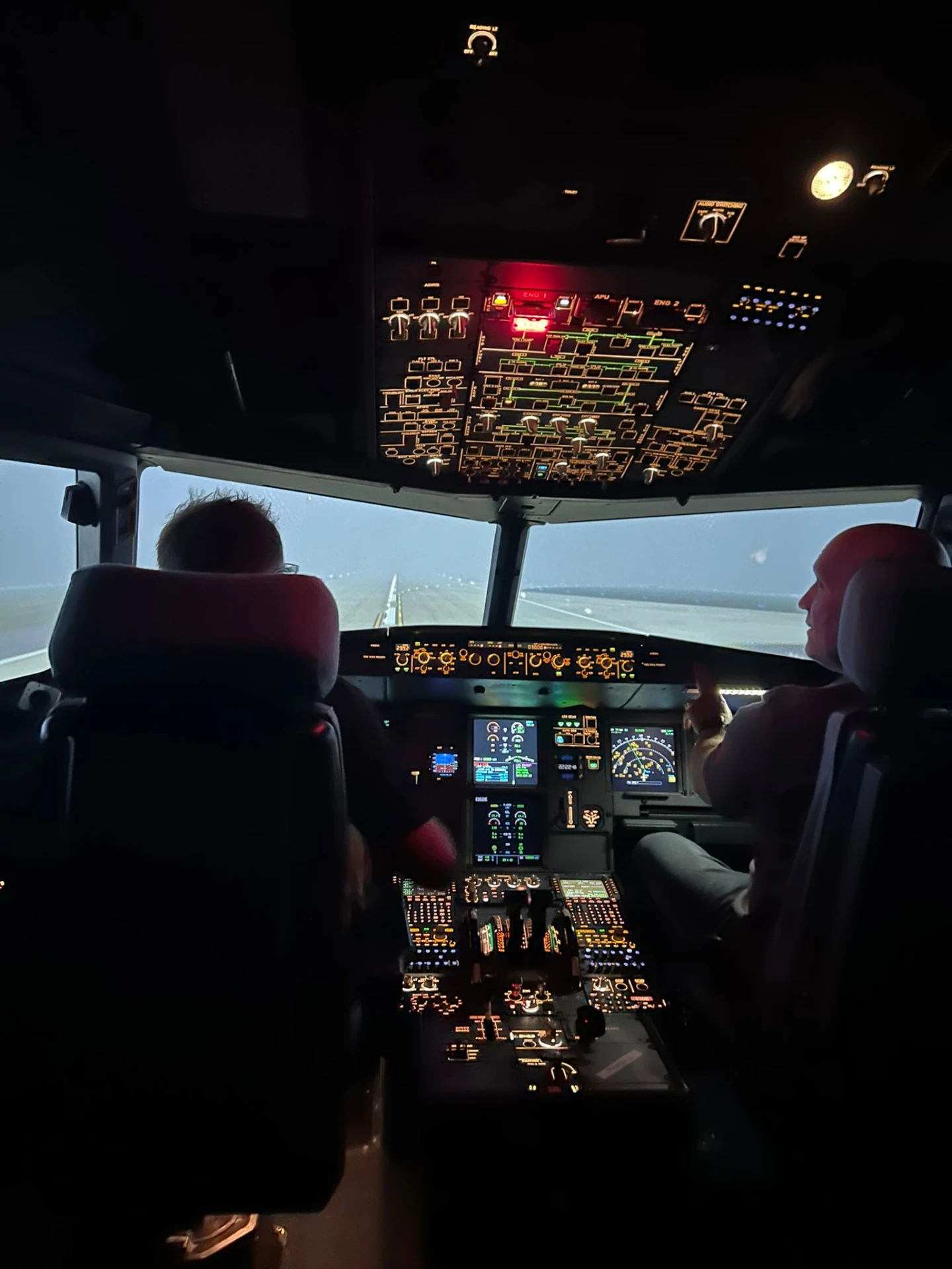 Two pilots in the simulator flight deck lining up on the runway at night