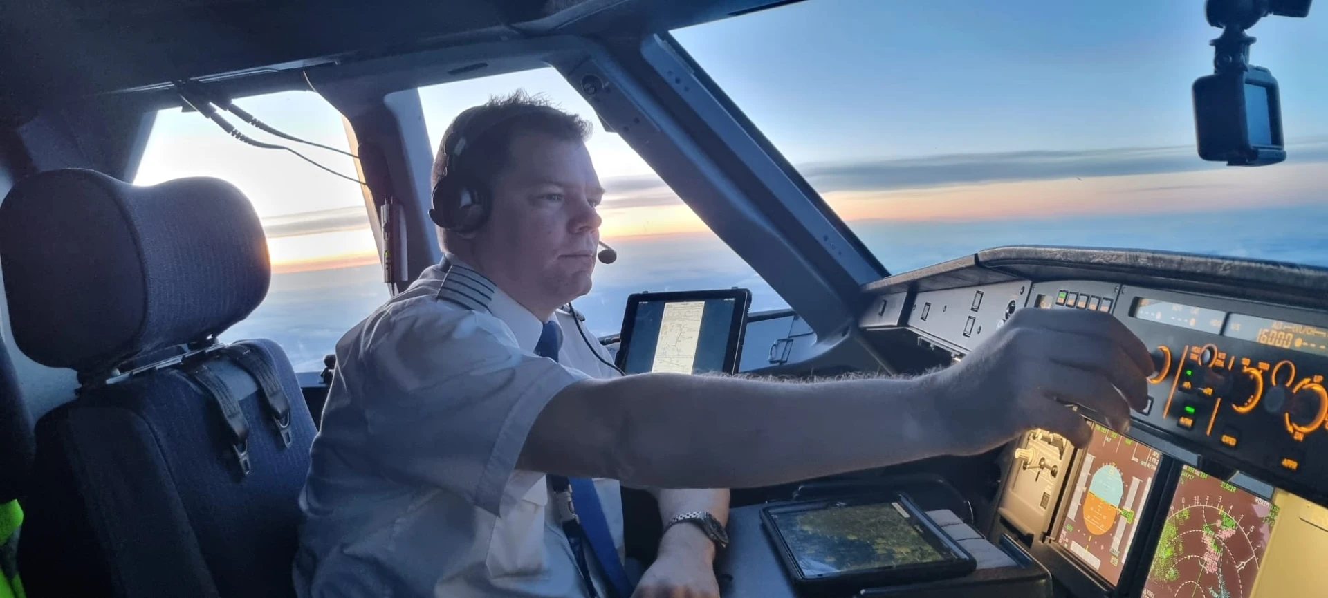 Pilot reaching for the autopilot panel at sunset