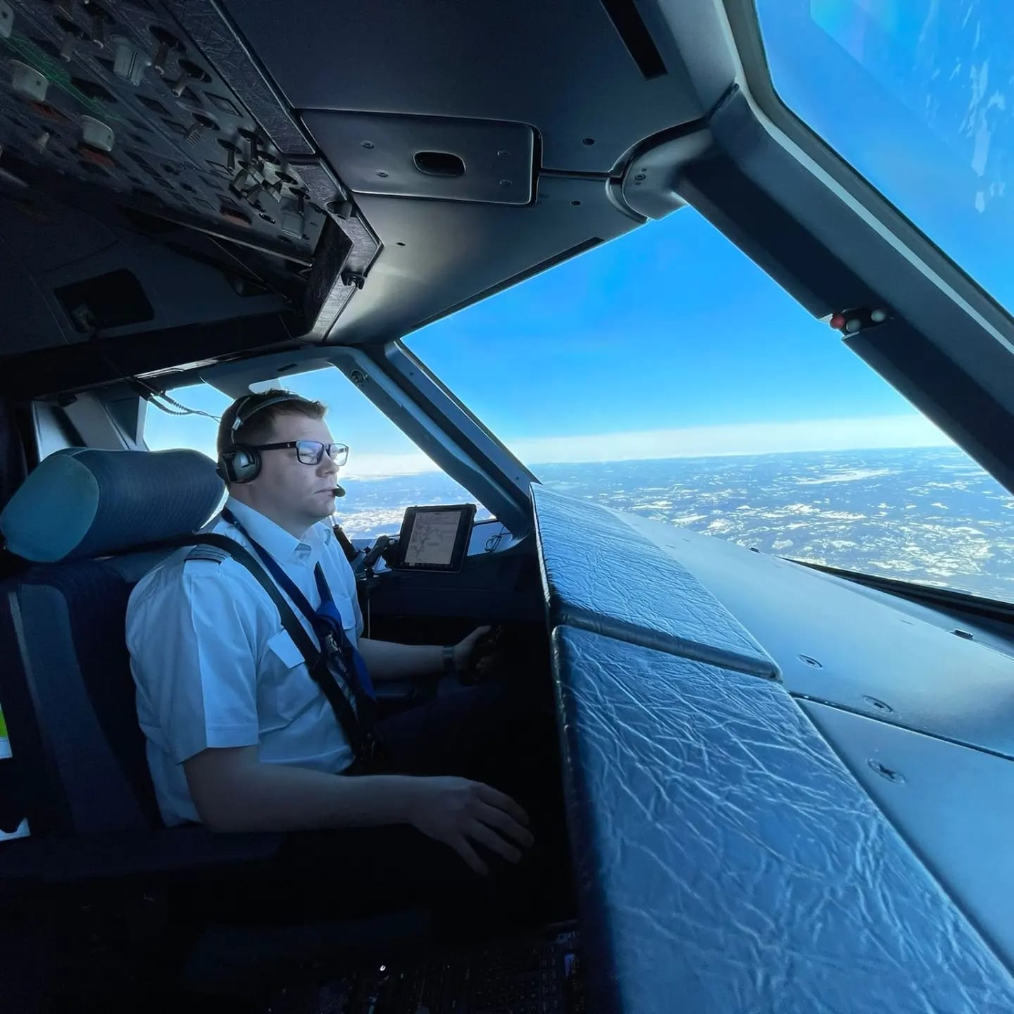 Pilot seated in the Airbus A320 flight deck looking out over the wing